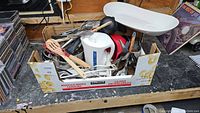 Mixed kitchen items in box including electric kettle, hand mixer, pots, and utensils