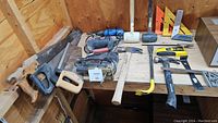 Overview of all tools arranged on a wooden surface showing hand saws, power tools, hammers, squares, and stud finder.
