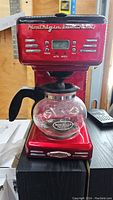 Front view of red Nostalgia coffee maker with glass carafe on base showing buttons and digital display