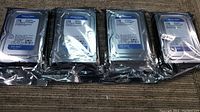 Four Western Digital Blue 1TB internal hard drives sealed in original anti-static packaging, placed side by side on a surface.