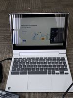 Front-facing view of open laptop showing keyboard, screen and attached power cable