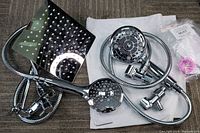 Two assembled shower head sets with hoses, connectors, and wall mounts laid out on carpeted surface and white cloth.