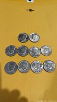 Ten vintage Kennedy Liberty Half Dollar coins displayed on a yellow background, arranged to show obverse side with John F. Kennedy profile.