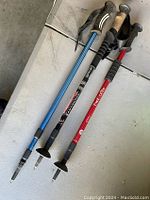 Photo of three assorted single walking sticks/trekking poles lying side by side showing different handles and shaft colors.
