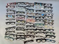 Overview of 60 assorted eyeglasses and reading glasses arranged in rows on a white surface showing variety in frame color and style.