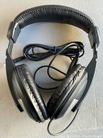 Single black over ear headphone with cushioned ear pads and headband, wired connection visible.