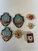 Seven assorted USSR pins, badges, and cockade displayed on a flat surface with clear view of shapes, colors, inscriptions and design details.
