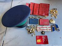 Photo of the vintage USSR military peaked cap, identity booklets, assorted pins, badges, parachute straps, epaulettes, and booklet spread on a table.