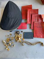 Photo displaying the black fabric hat, multiple red and blue identity cards, a variety of small pins and badges including star shapes and a chain.