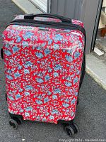 Front view of red floral hard-shell carry-on suitcase with wheels on pavement