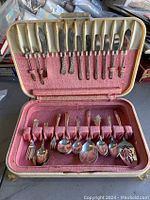 Open box showing an assortment of knives, forks, spoons, and serving utensils in velvet slots.