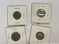 Top view of four Buffalo Nickel coins in white cardboard holders with plastic windows showing the coins' obverse sides.