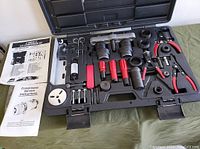 Photo showing black plastic case open with organized red and black handled tools, white circular part, and two instruction booklets.