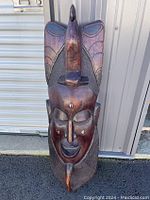 Front view of the large hand-carved wooden mask with painted details and textured, raised features.