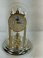 Full view of the Concordia anniversary clock under a glass dome with gold-tone metal base and decorative pendulum.