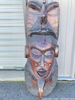Front full view of the tall wooden African tribal mask with detailed face and bird figure on top.