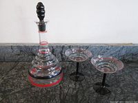 Overall view of the hand painted Art Deco glass decanter with a solid black stopper and two matching martini glasses with black stems and red rings on the bowls.