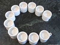 11 white ceramic IKEA tea light candle holders arranged in a circular linked pattern on a dark surface, showing their interlocking capability.