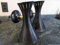 Pair of black metal Mid Century wall sconces shown side by side, highlighting their shape and sizes with conical shades and circular wall plates.