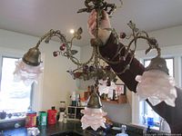 Chandelier held hanging by a person showing all four pink glass rose-shaped shades and brass framework with purple glass ball accents.