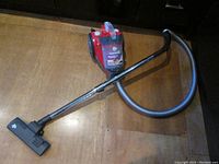 Full view of the red Dirt Devil Featherlite canister vacuum cleaner with black hose and floor head on wooden surface.