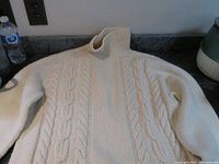 Cream-colored hand knit Aran fisherman’s sweater laid flat showing cabling pattern and roll neck.