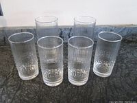 Front-angle view of six clear glass tumblers with vertical ribbing and bubble texture near base on dark marble surface.