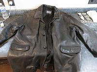 Front view of a vintage black leather jacket with button closure, two front flap pockets, and collar, laid flat on a surface.
