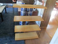 Full frontal view of the shelving unit held by a person, showing all four wood shelves and metal rails.