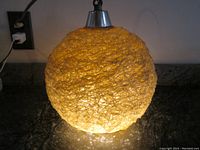 Front view of the glowing MCM spaghetti pendant lamp on a dark surface, showing the warm amber light through the textured spaghetti strand shade.