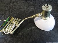 Close-up of lamp showing polished brass scissor arm, wiring, and white lamp shade with perforated metal detail on lamp head.