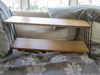 Full front view of the mid century modular shelving/bookcase showing two wooden shelves supported by black metal side rails on a fabric surface.