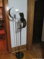 Full view of the mid century modern floor lamp against wall, showing three vertical light rods with bulbs and semicircular reflector panels.