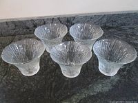 Five clear glass votive or tea light holders arranged side by side on a surface.