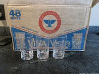 Three clear glass juice glasses shown in front of the original retail display box labeled 'Ravenhead Viva Vista 48 Pieces'. Glasses have a textured geometric pattern and thick glass base.