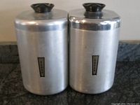 Two spun aluminum kitchen canisters side by side, showing overall shape, size, and Bakelite handles on lids.