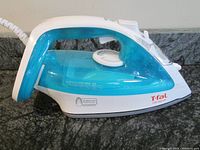 Side view of the turquoise and white Tfal Ultraglide steam iron with temperature dial and water reservoir.