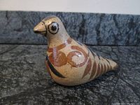 Ceramic bird figurine side angle showing decorative swirls and speckled texture.