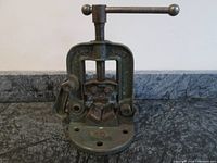 Front view of the pipe vise showing the screw and base with mounting holes on a textured surface.