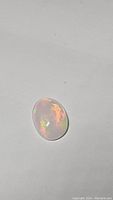 Oval cabochon fire opal against white background showing orange and red internal flashes.