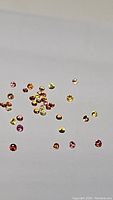 Scattered round cut multicolored sapphires in varying shades including red, pink, orange, yellow, and light green on a white background.