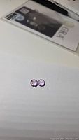 Pair of small round purple pink amethyst gemstones, placed on white surface.