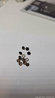Close-up photo of 15 small round calibrated smokey quartz gemstones with faceted cuts on a white background.