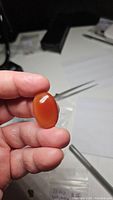 Closeup photo of hand holding a large deep red-orange oval cabochon carnelian gemstone showing glossy polished surface.