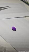 Photo of 9.21 ct deep purple amethyst gemstone on white background with tweezers visible, showing overall oval shape and color