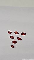 Seven marquis cut deep fire orange-red sapphires on a white background showing color and clarity.