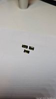 Three small rectangular cut green tourmaline gemstones on white paper surface shown from a distance.