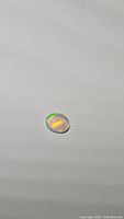 Close-up photo of oval cabochon cut opal with visible green and orange color flashes.