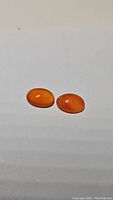 Pair of smooth oval mandarin orange carnelian gemstones on white background, showing bright orange color.