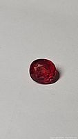 Close-up of the deep red-orange cushion cut sapphire gemstone on a light background.